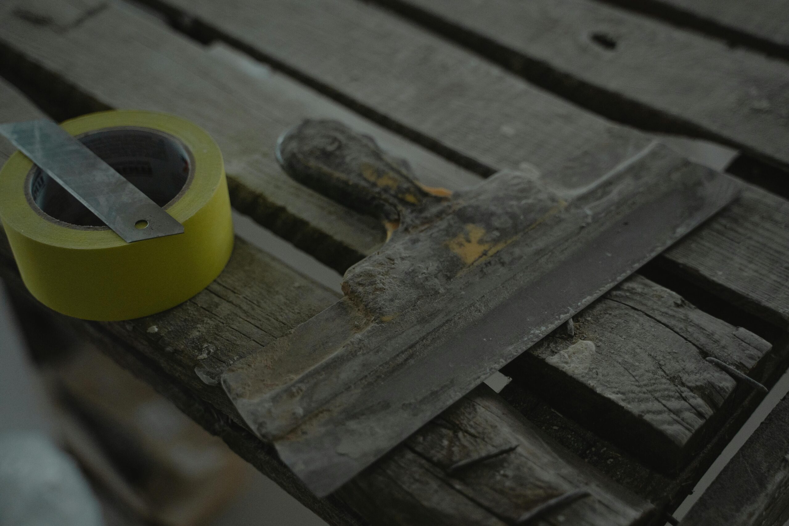 Close-up of a spatula and duct tape on an aged wooden surface. Perfect for DIY and renovation themes.